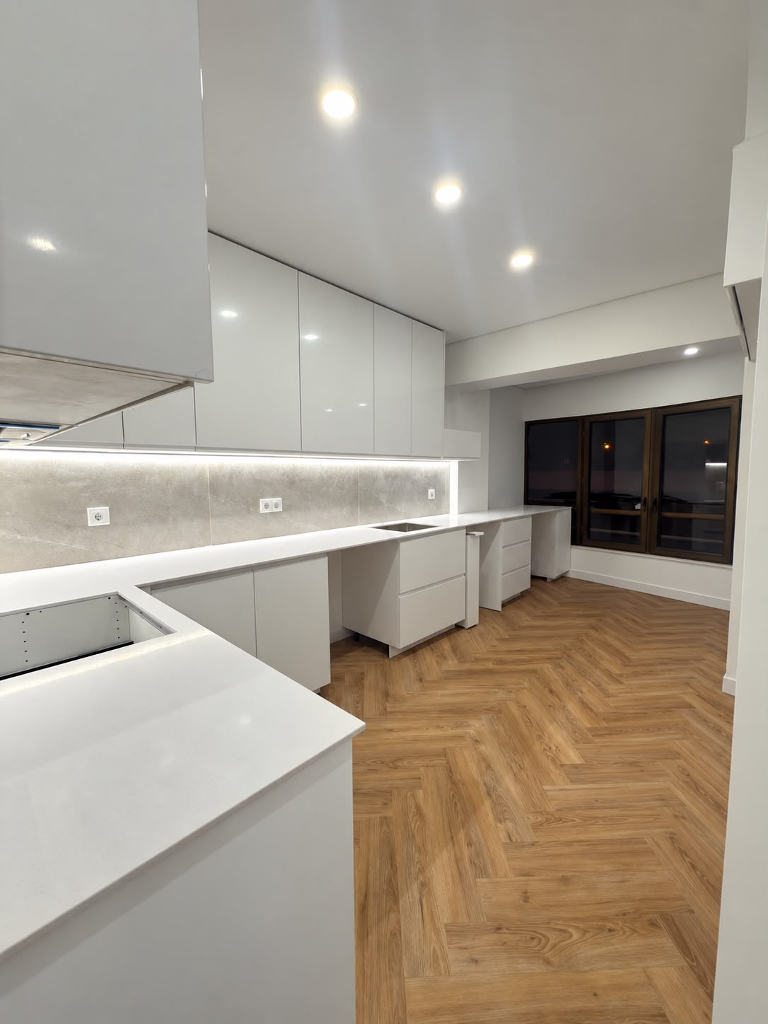Cozinha renovada com armários brancos, bancada clara e pavimento em madeira